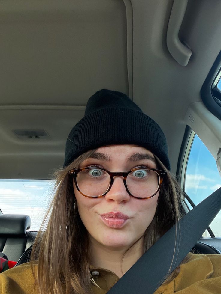 a woman wearing glasses and a beanie in the back seat of a car