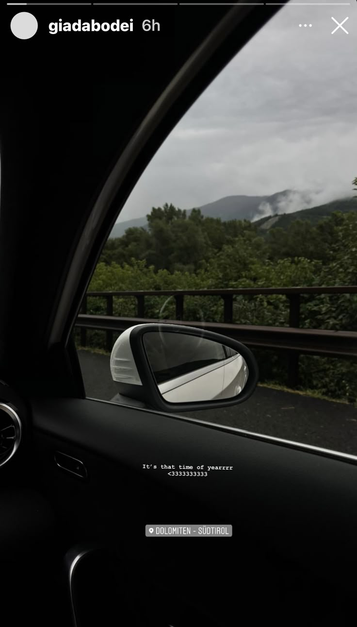 a car's side view mirror with mountains in the back ground and trees behind it