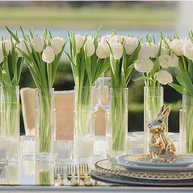 there are many vases with white flowers in them on the dining room table set for dinner