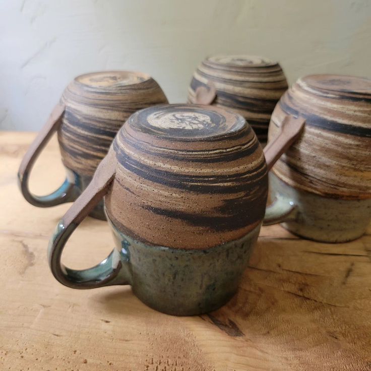 three coffee mugs sitting on top of a wooden table next to each other with handles