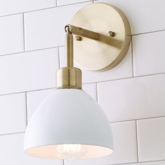 a light fixture on the wall above a sink in a white tiled bathroom with gold fixtures