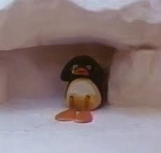 a small toy penguin sitting in the corner of an ice cave with snow on the ground