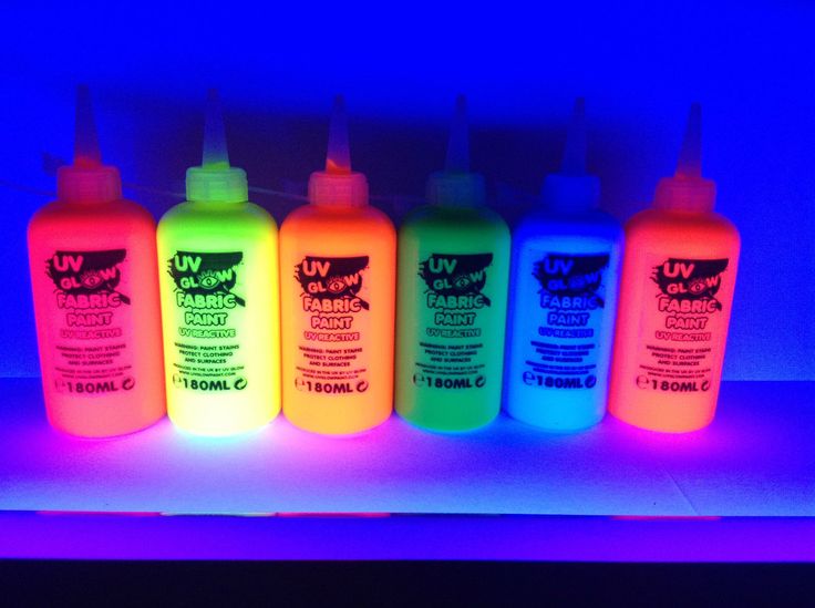 four bottles of neon colored fluorescent ink on a shelf in front of a blue light