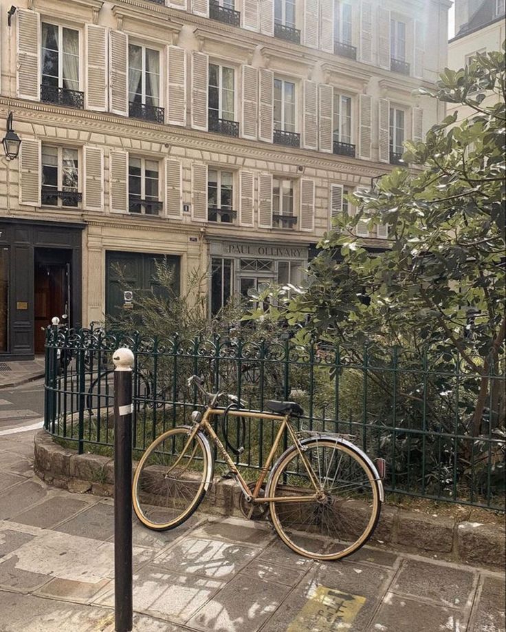 a bicycle parked on the side of a street next to a fence and building with lots of windows