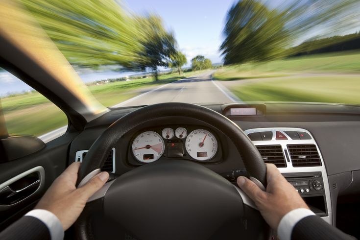 a person driving a car on a road with blurry trees in the back ground