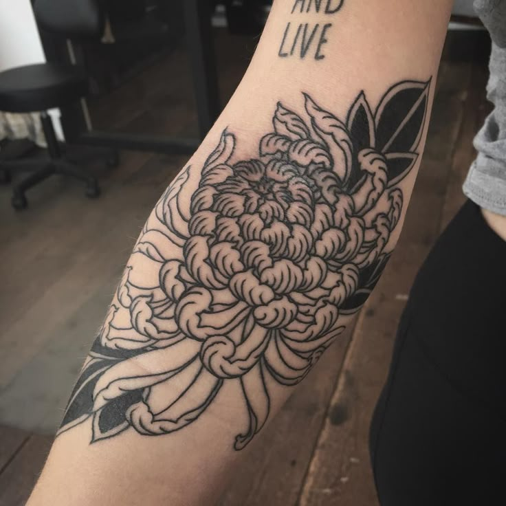 a woman with a tattoo on her arm that says and live in black ink, sitting next to a table