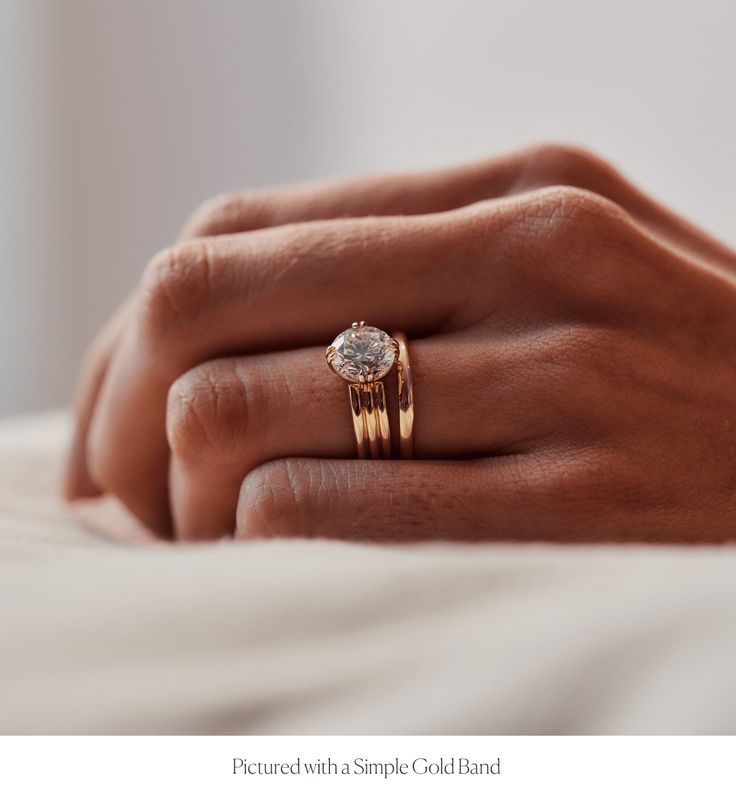 a woman's hand with two gold rings on her left and the other hand holding an engagement ring