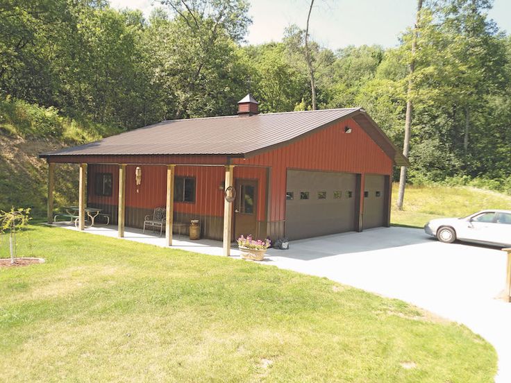 a car is parked in front of a red barn with a garage attached to it