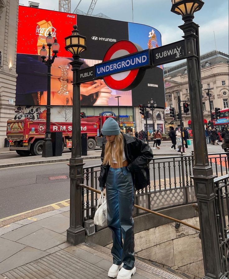 a woman standing on the sidewalk next to a pole with a sign that says underground