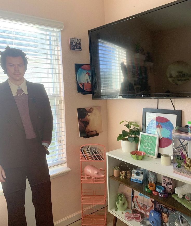 a man standing in front of a flat screen tv next to a shelf with various items on it