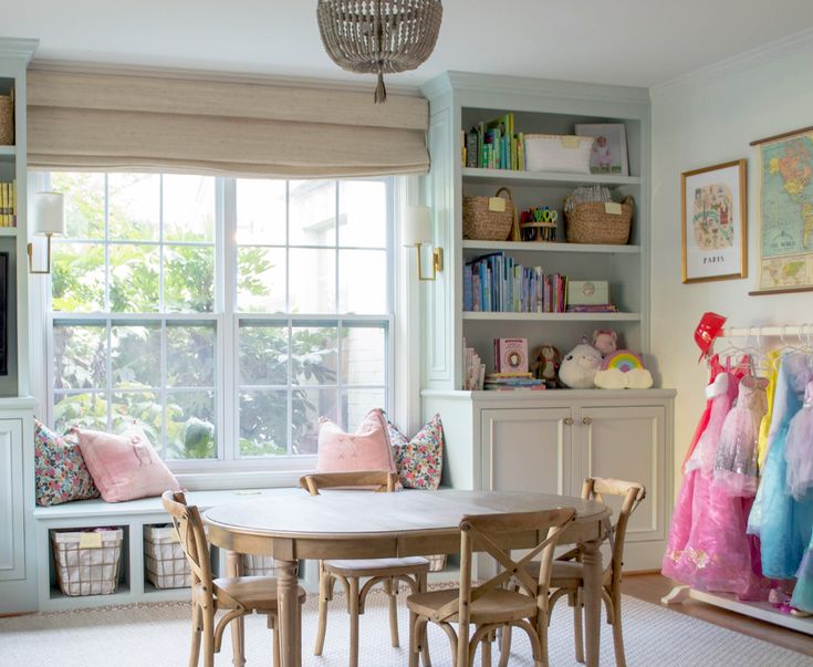 a dining room table and chairs in front of a window with bookshelf behind it