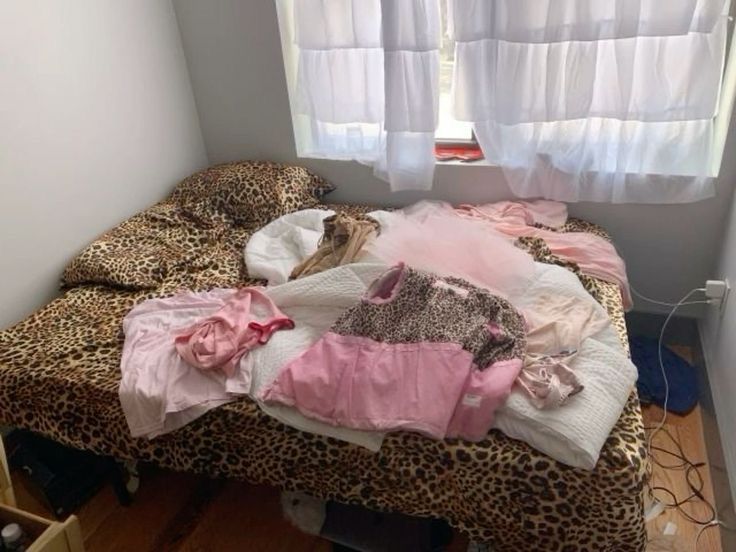 an unmade bed with leopard print sheets and clothes on it in front of a window