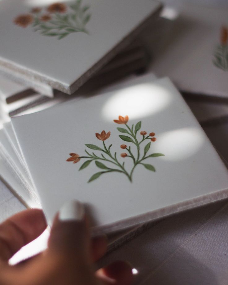 a person holding a white object in front of four square tiles with orange flowers on them