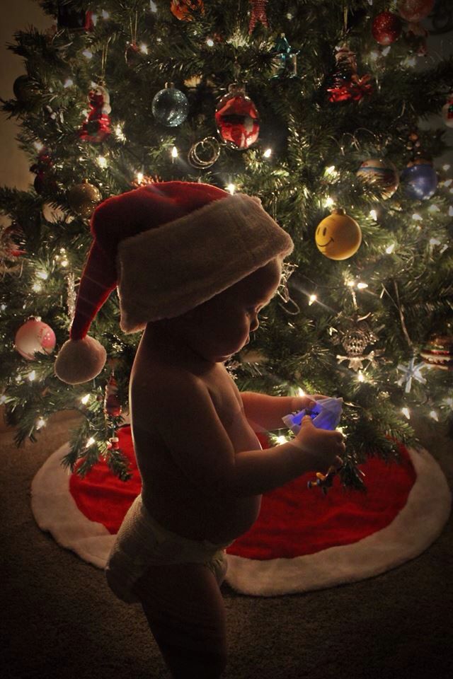 a baby wearing a santa hat standing in front of a christmas tree with ornaments on it