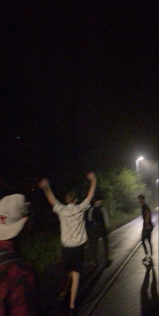 a group of people standing on the side of a road at night with their arms in the air