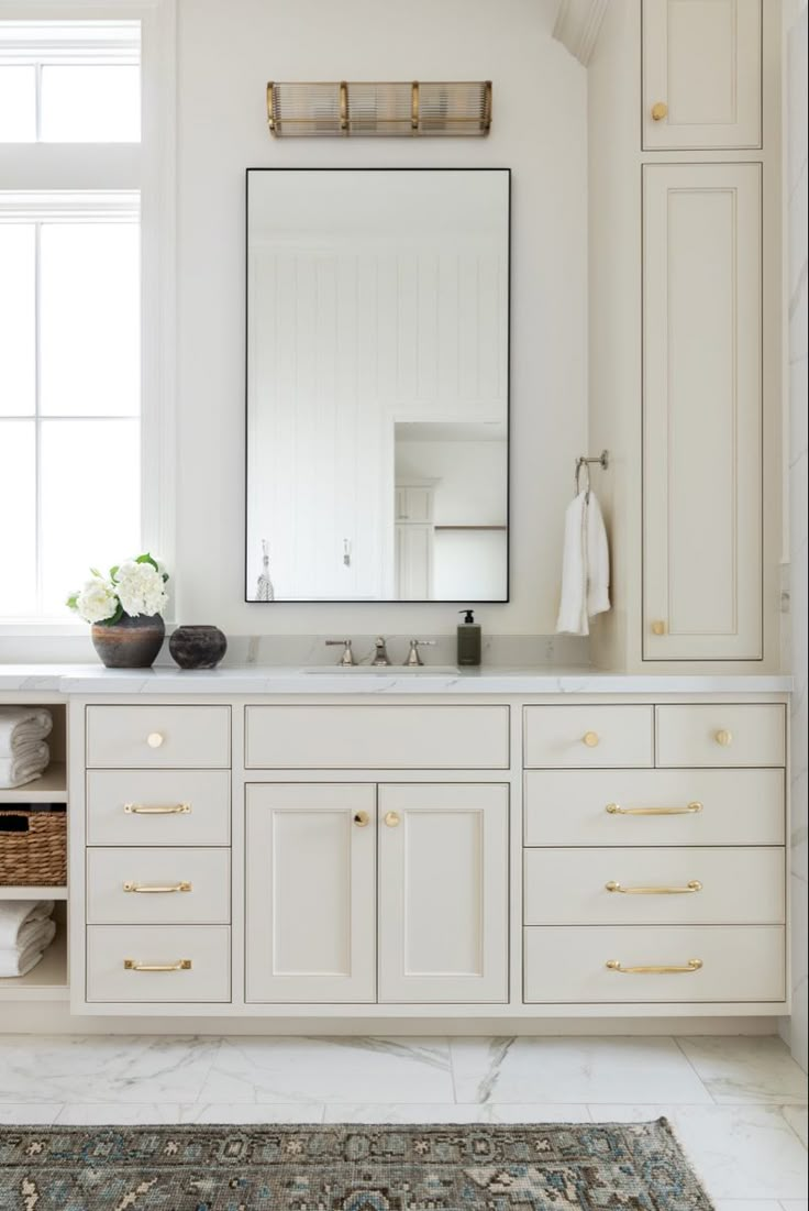 a bathroom with white cabinets and a large mirror above the sink, along with a rug on the floor