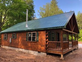 a log cabin sits in the middle of a wooded area with a green roof and porch