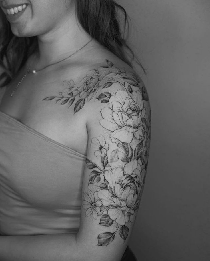 a woman with a flower tattoo on her arm and shoulder, smiling at the camera