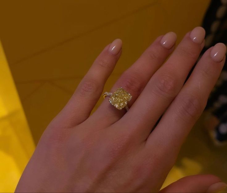 a woman's hand with a yellow diamond ring on top of her left hand