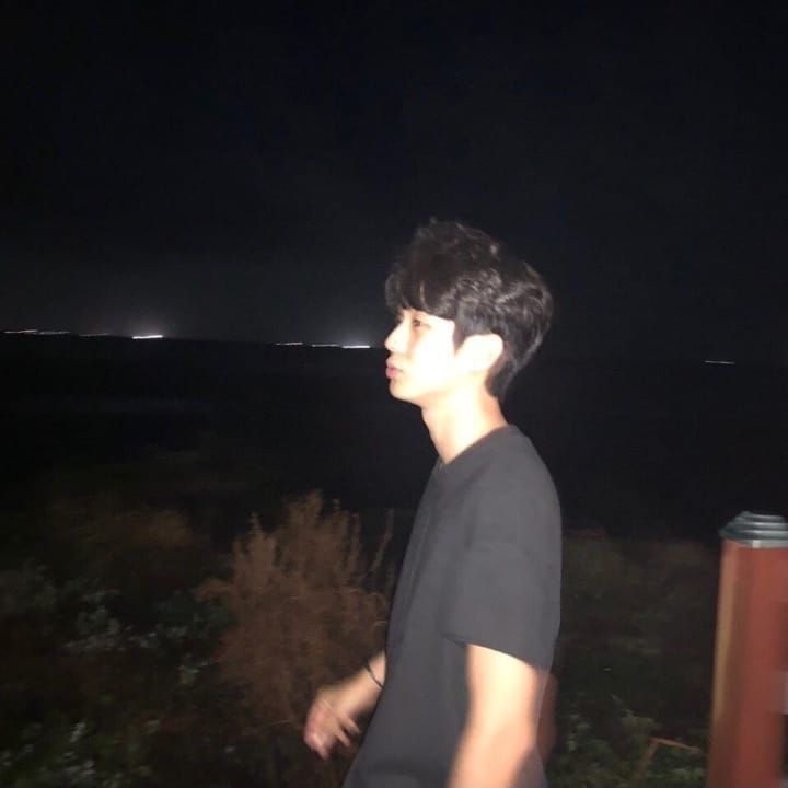 a young man standing on top of a lush green field next to the ocean at night