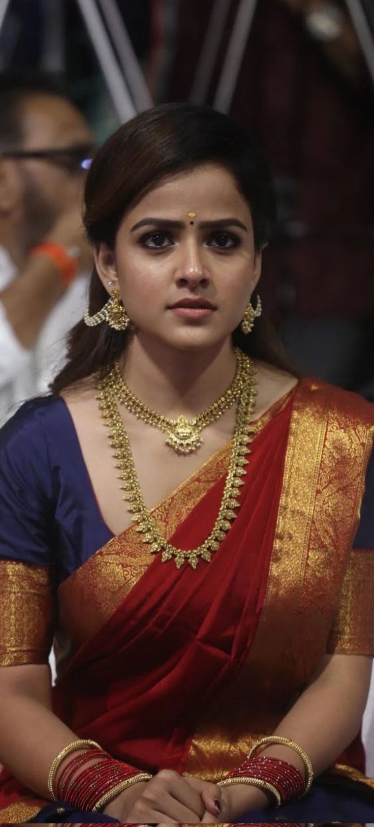 a woman in a red and blue sari with gold jewelry on her neck is looking at the camera