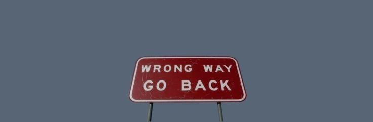 a red and white sign that says wrong way go back in front of a gray sky