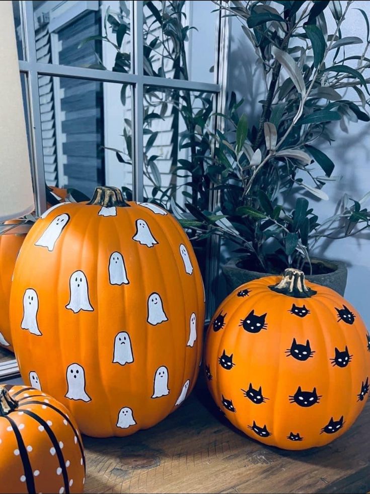 three pumpkins with ghost faces and black cats on them sitting on a table next to a potted plant