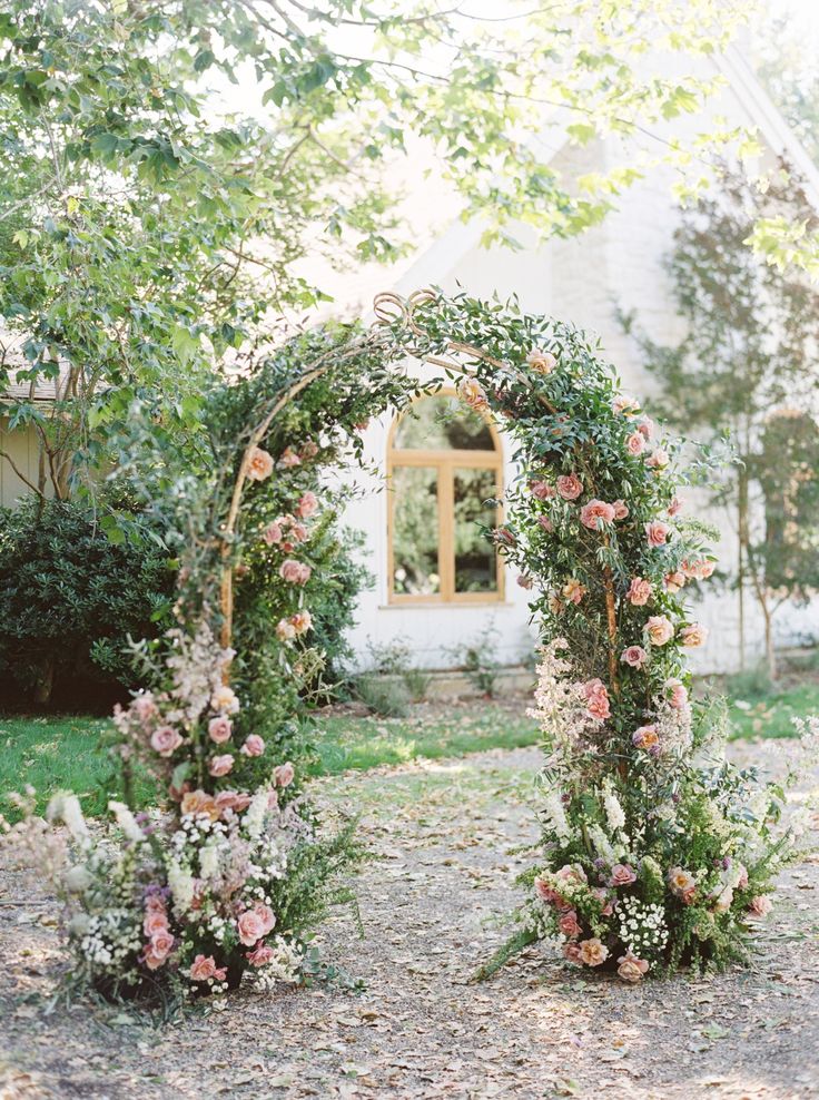 an outdoor wedding ceremony with flowers and greenery on the arch, in front of a white house