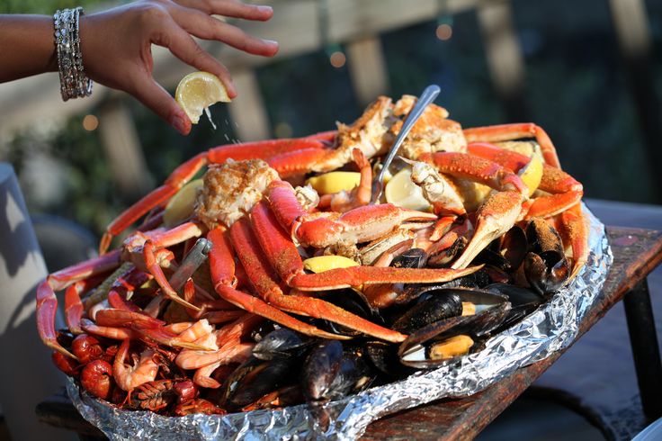 a pile of crab and shellfish on top of tin foil with a person reaching for it