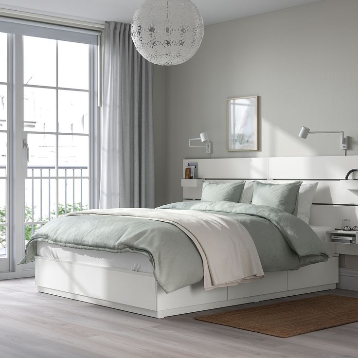 a white bed sitting next to a window in a room with wooden floors and gray walls