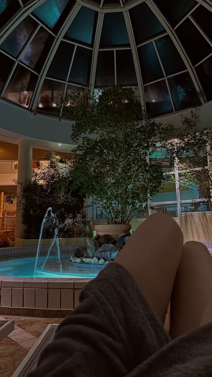 a person's feet resting in front of a pool with a fountain at night