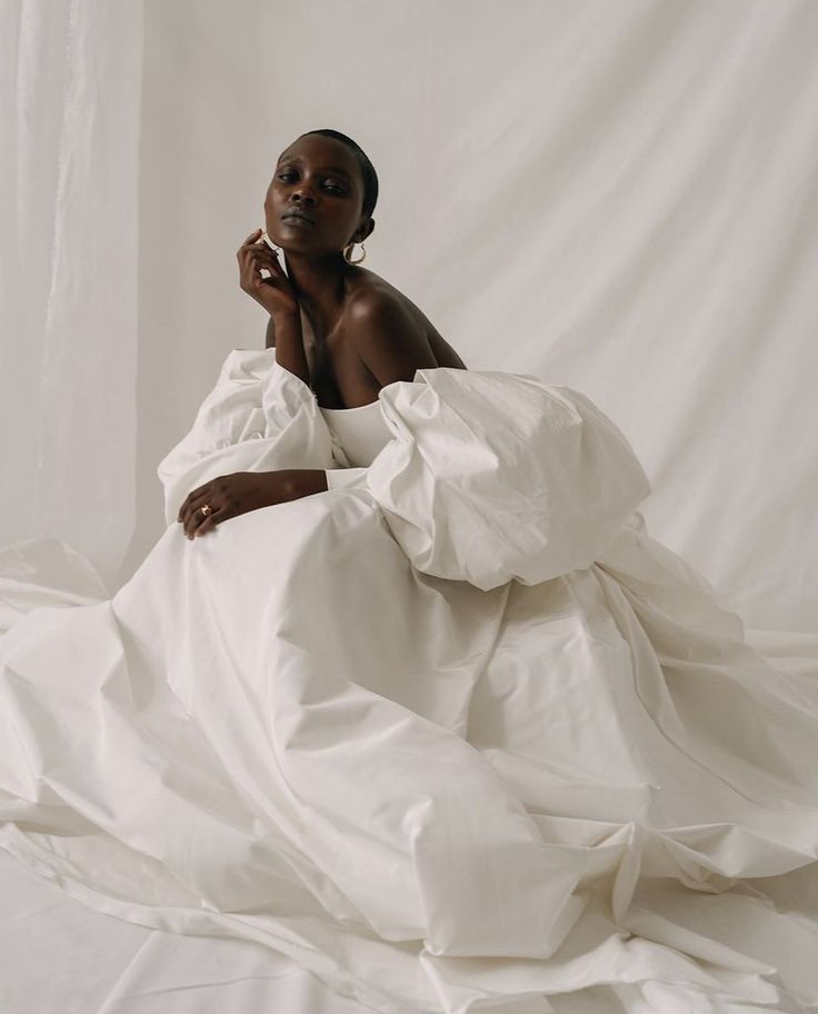 a woman is sitting on a bed covered in white sheets and blankets with her hand under her chin