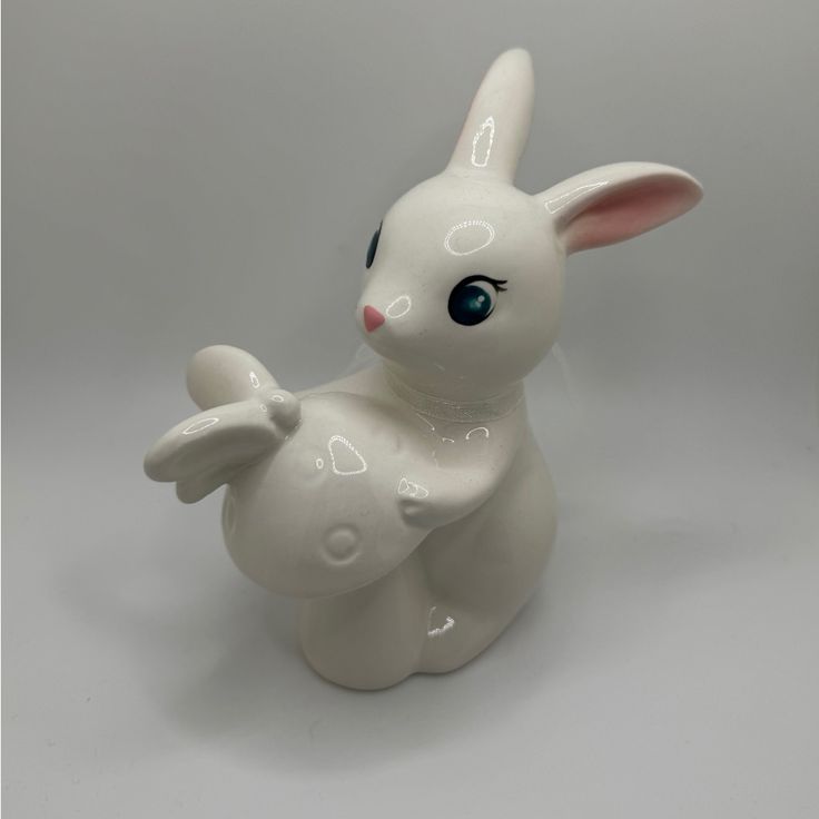 a white ceramic rabbit figurine sitting on top of a gray surface with blue eyes