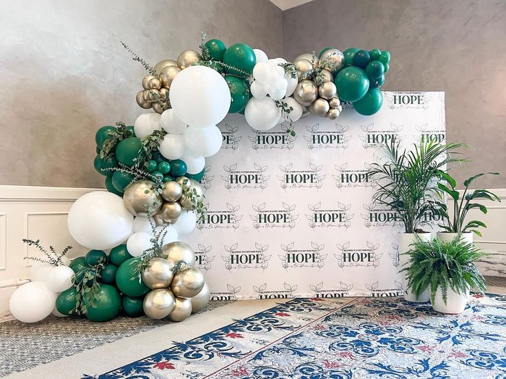 a balloon arch is decorated with green, white and gold balloons for a holiday party