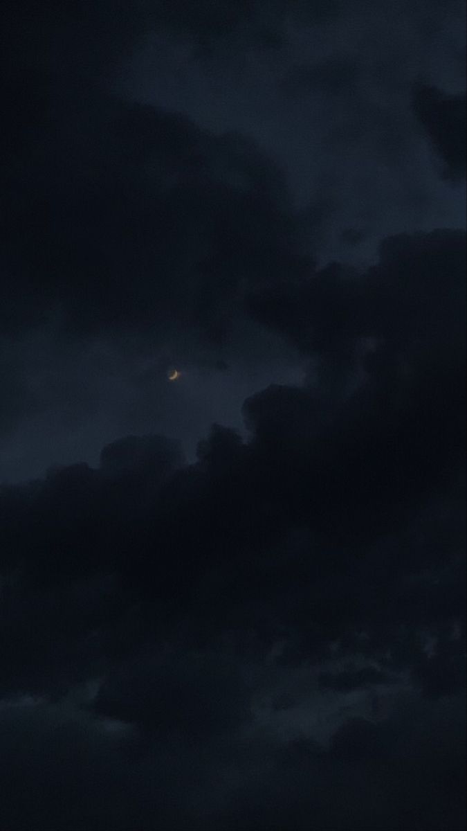 the moon is seen through dark clouds in the night sky, with only one light visible