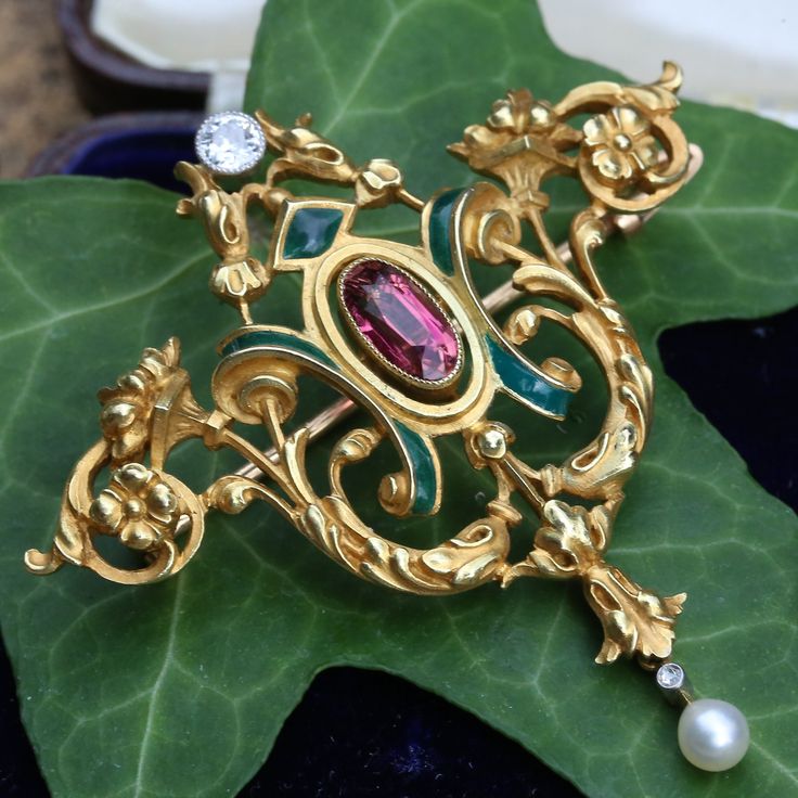 This is a French Art Nouveau 18ct yellow gold brooch pendant. The highly decorated, iconic Art Nouveau frame has a floriated design, composed of beautifully enameled sections and a pink tourmaline in the centre. There is also an old cut diamond at the top and a single natural pearl moving freely at the bottom. The brooch features 2 loops in which a chain could be attached to make it a wonderful pendant. The pin also unscrews from the back. It is an impressive 15.5 grams and exemplifies beautiful Luxury Gold Enamel Brooch, Luxury Gold Enamel Brooches, Yellow Gold Enamel Brooches Hallmarked, Luxury Gold Brooches With Intricate Design, Baroque Yellow Gold Brooch Jewelry, Luxury Gold Enamel Pin As Gift, Luxury Gold Enamel Pin Gift, Luxury Gold Enamel Pin For Gift, Baroque Yellow Gold Brooch