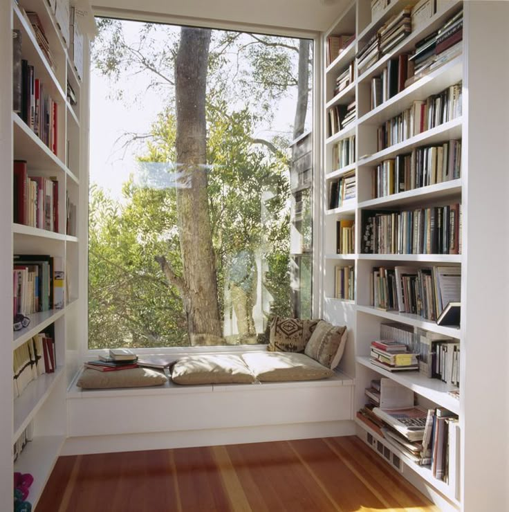 a window seat in the corner of a room with bookshelves full of books