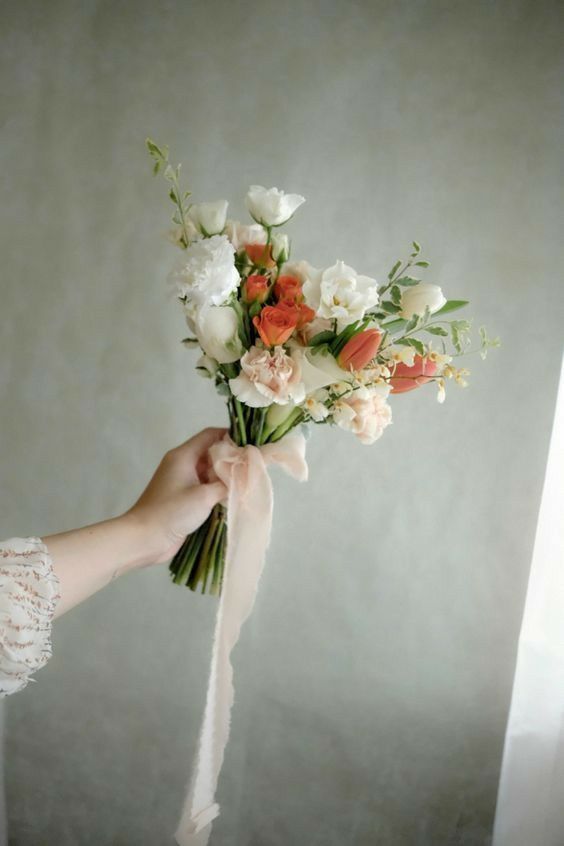 a person holding a bouquet of flowers in their hand with a white ribbon around it