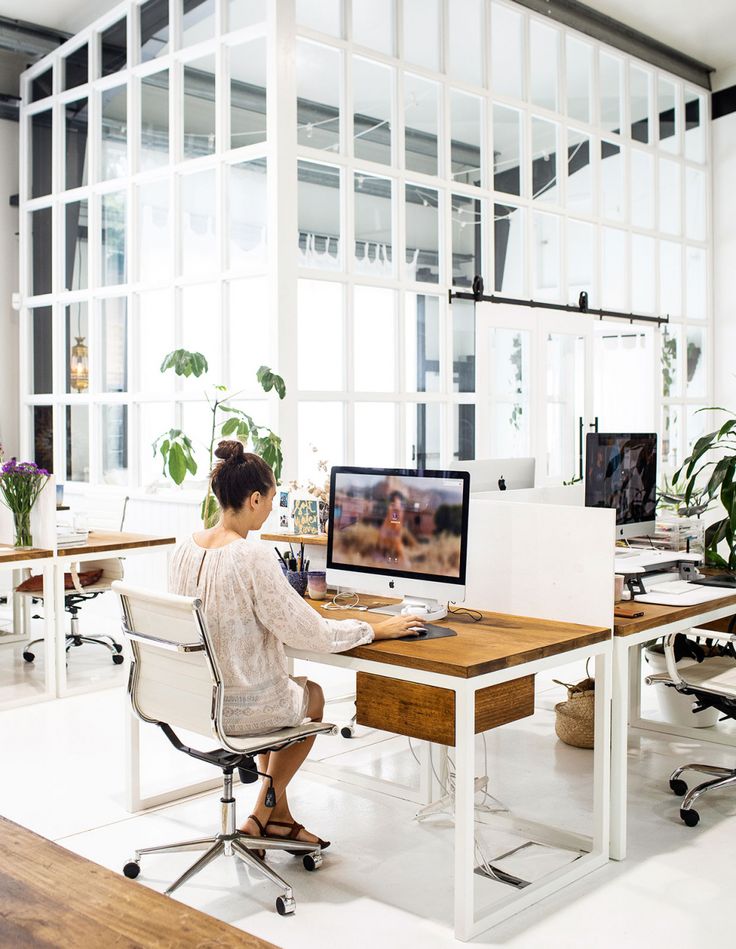 a woman sitting at a desk in front of a computer monitor on top of a wooden table