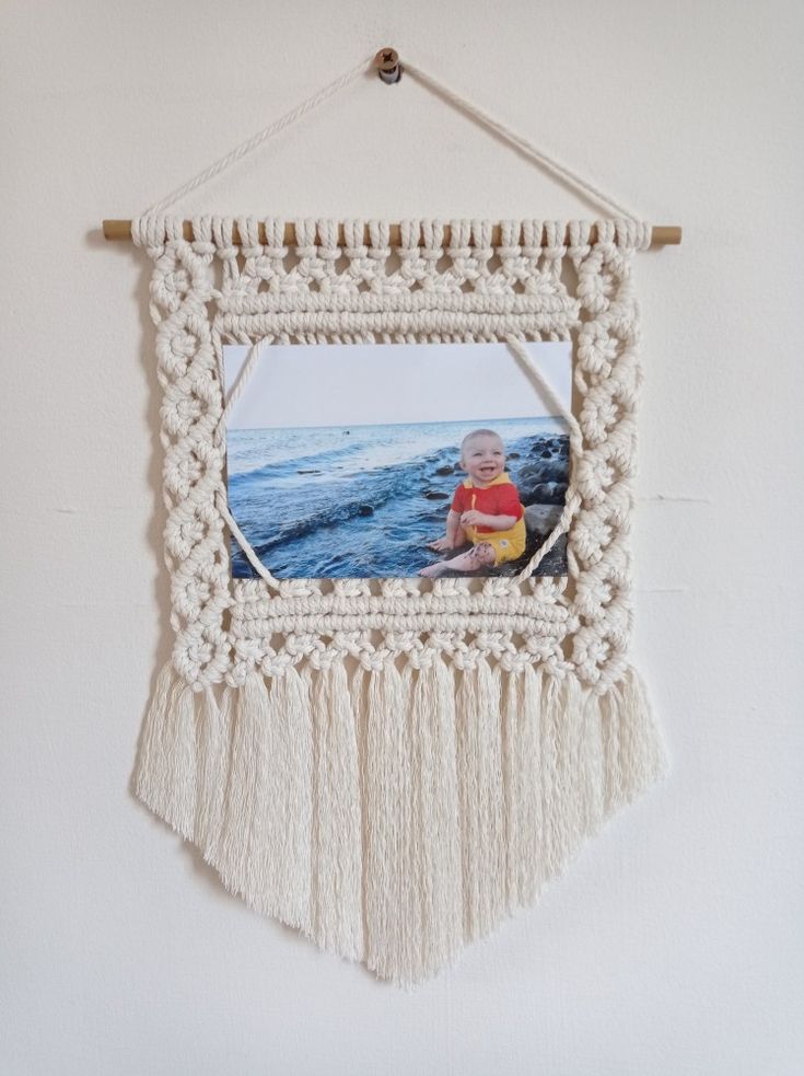 a white wall hanging with a photo frame and tassels on the bottom half