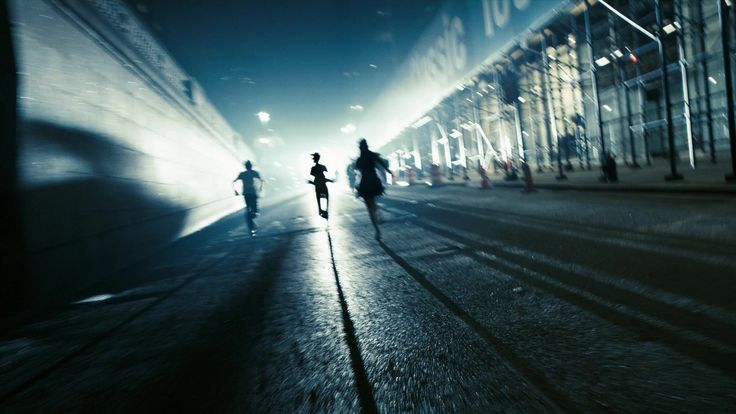 three people are running down the street in the dark, with shadows on the ground