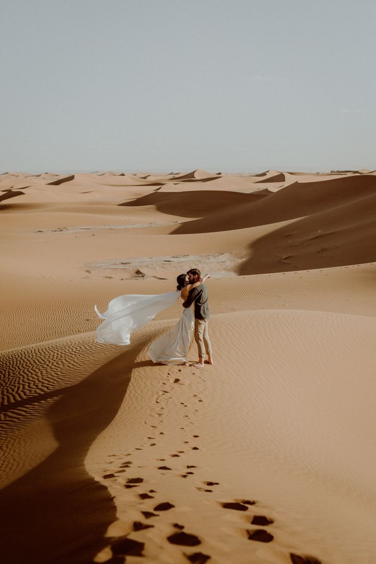 a man and woman are standing in the sand with their arms around each other as they kiss