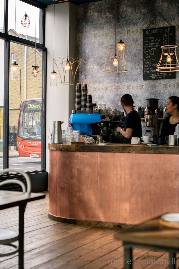 two people sitting at a counter in a coffee shop next to an open window with a bus passing by