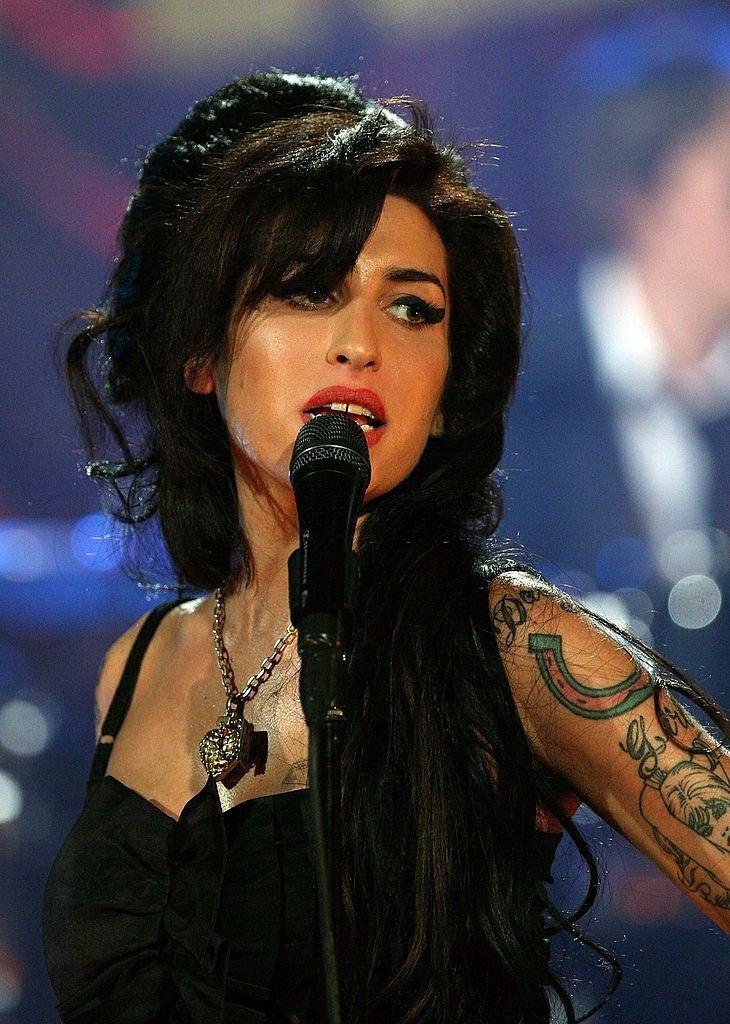 a woman with long black hair and tattoos on her arm holding a microphone in front of an audience