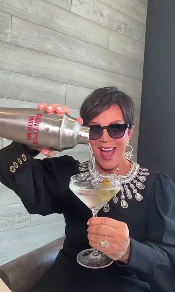 a woman sitting in a chair holding a martini glass and pouring it into her mouth