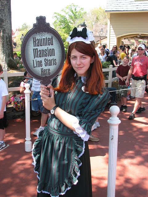 a woman dressed in costume holding up a sign that says haunted mansion line starts here