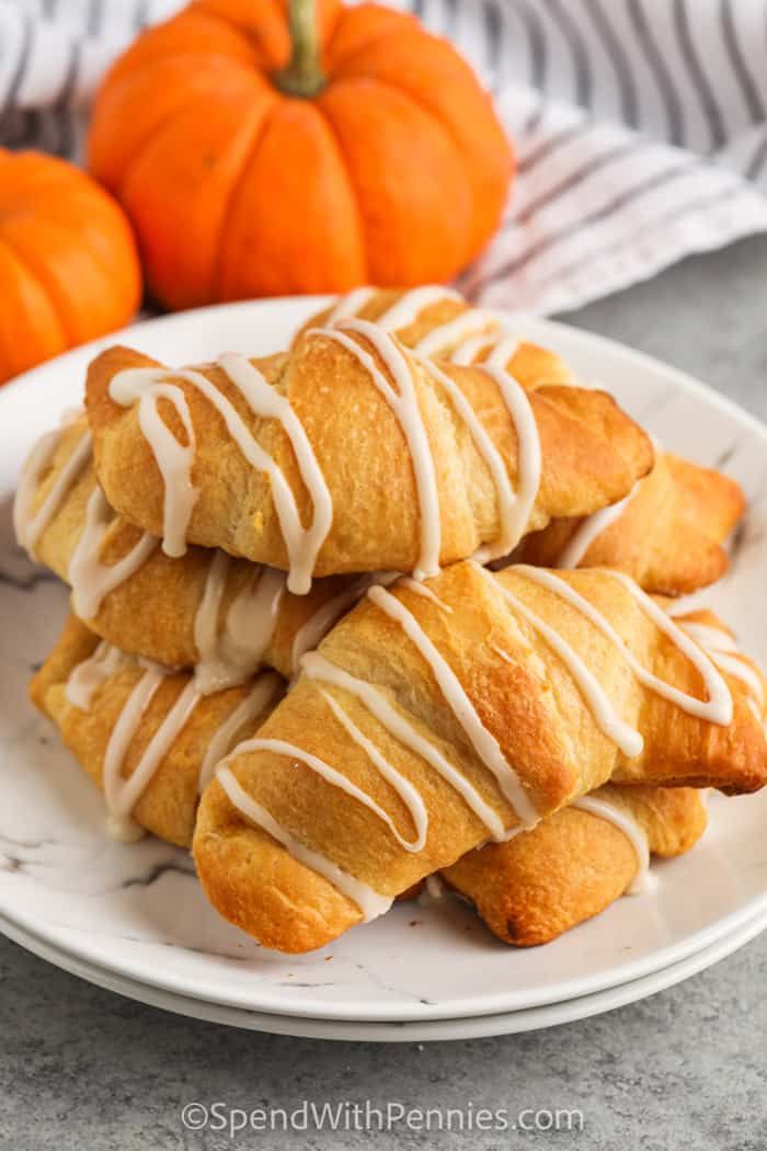 a white plate topped with cinnamon rolls covered in icing next to pumpkins on a table