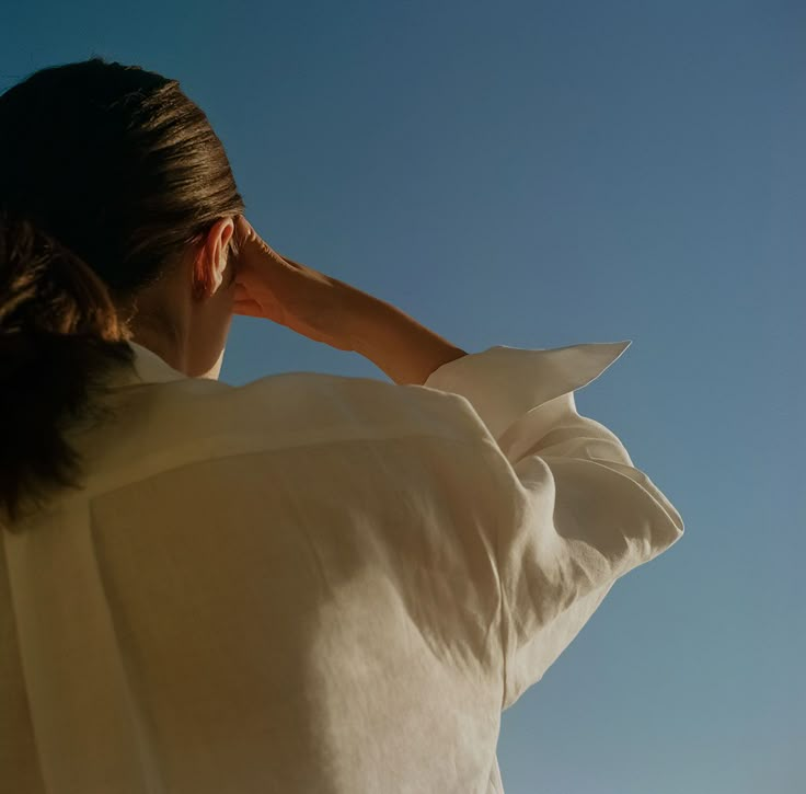 a woman in a white shirt is looking up at the sky