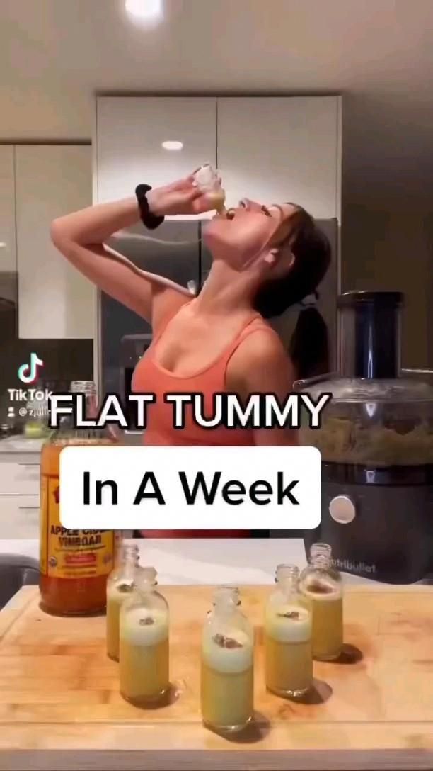 a woman drinking from a bottle while standing in front of some jars on a counter