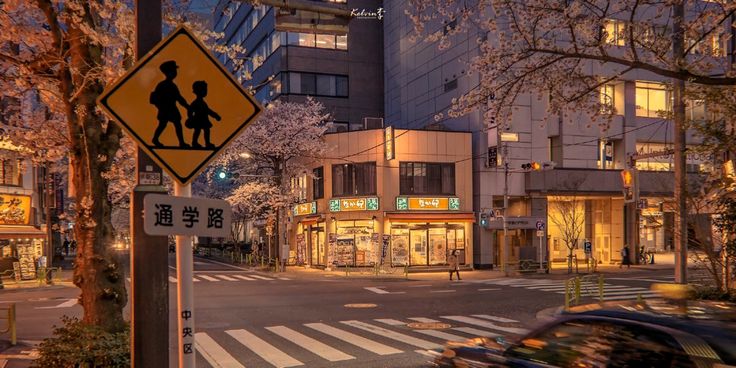 a yellow pedestrian crossing sign sitting on the side of a road next to tall buildings